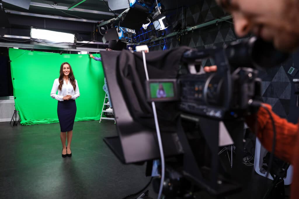Cameraman pointing camera at businesswoman in front of a green screen